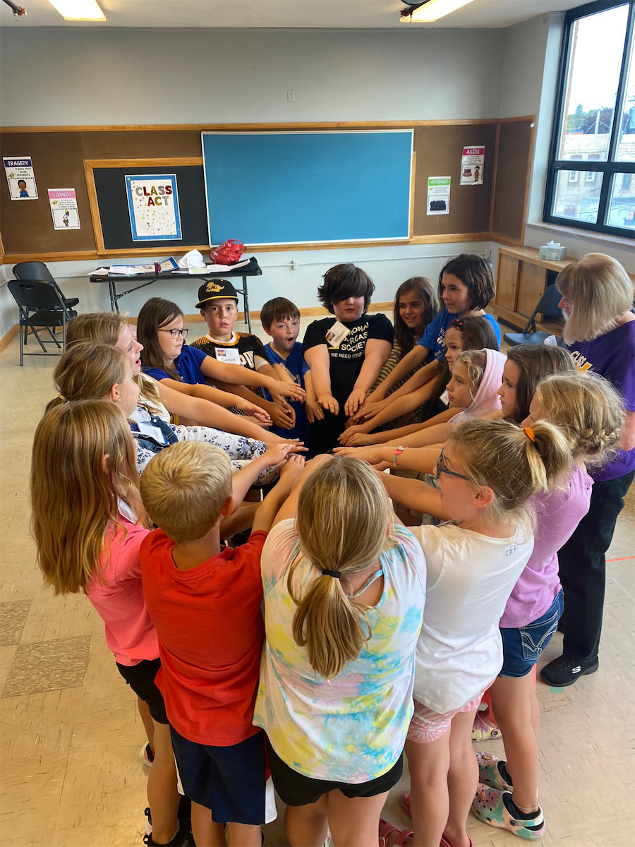 Children gathered around all putting their hands into a circle