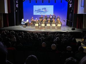 View of band on stage with audience in the foreground.